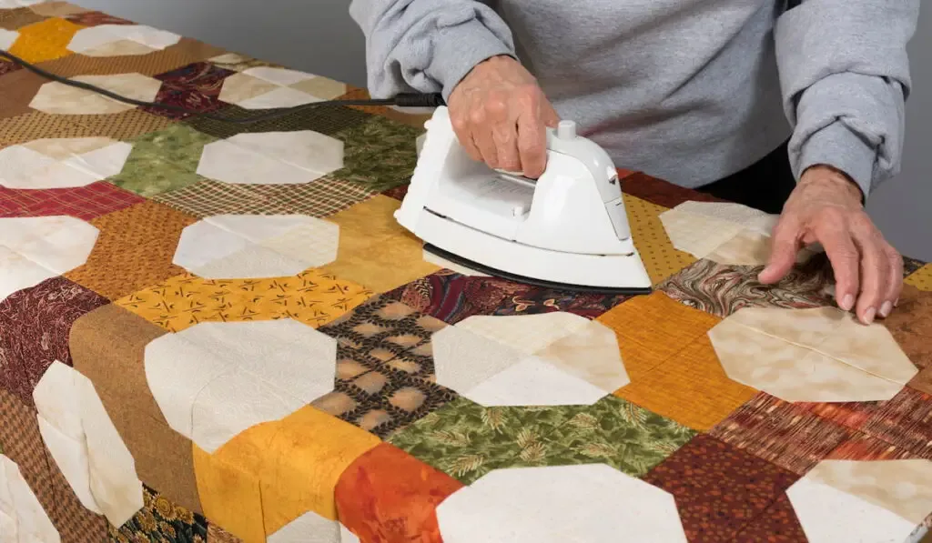 A quilter uses and iron to smooth out and press out any wrinkles on a bow tie quilt top.