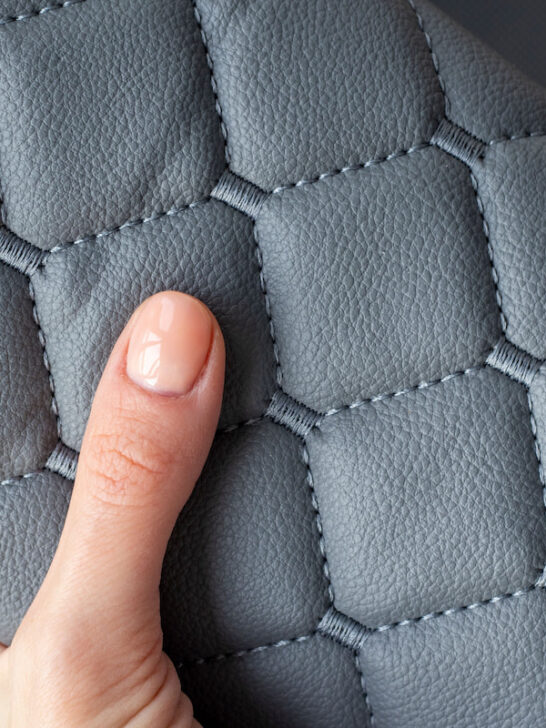 hand holding a roll of gray quilted leather fabric