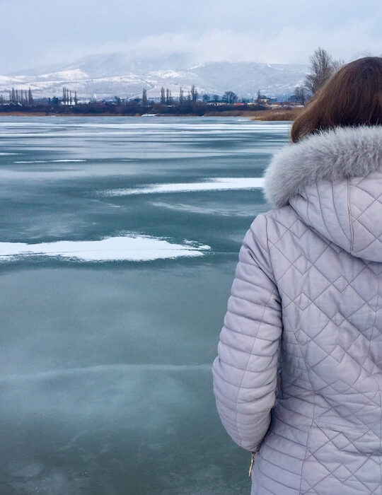 back-of-woman-wearing-light-purple-winter-jacket-near-a-frozen-lake
