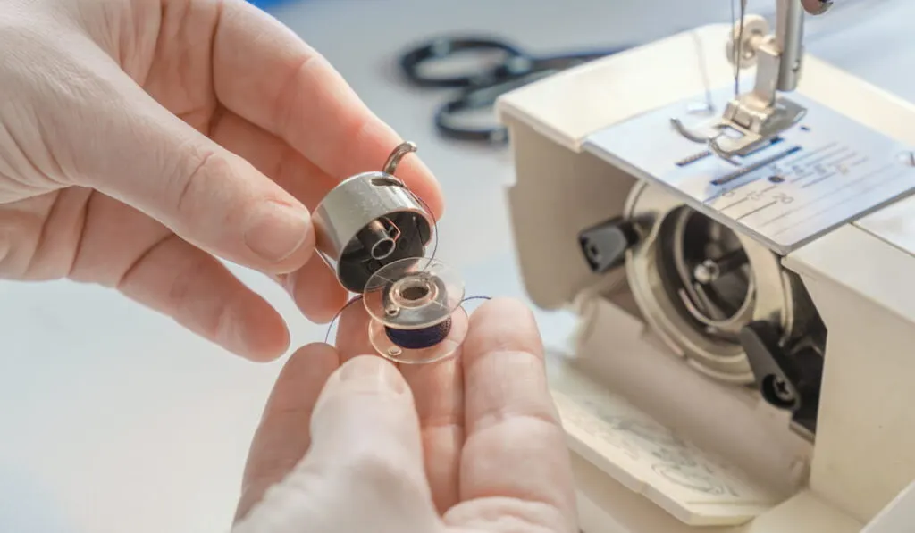 Female hands hold a metal bobbin case and bobbin on the background of a sewing machine