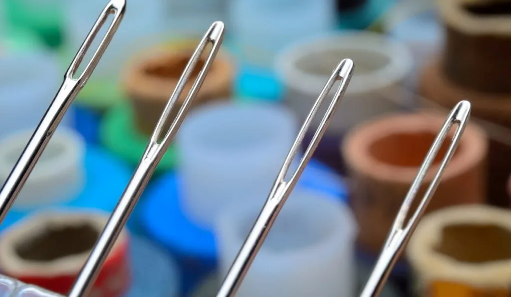 Four sewing needles on a background of spools of thread