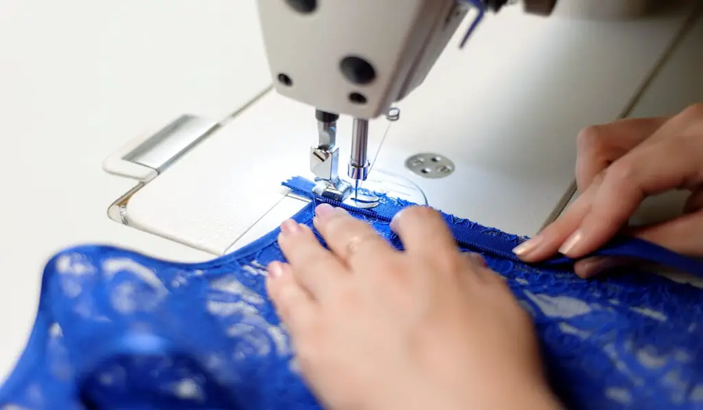 Hands of a woman sewing blue fabric