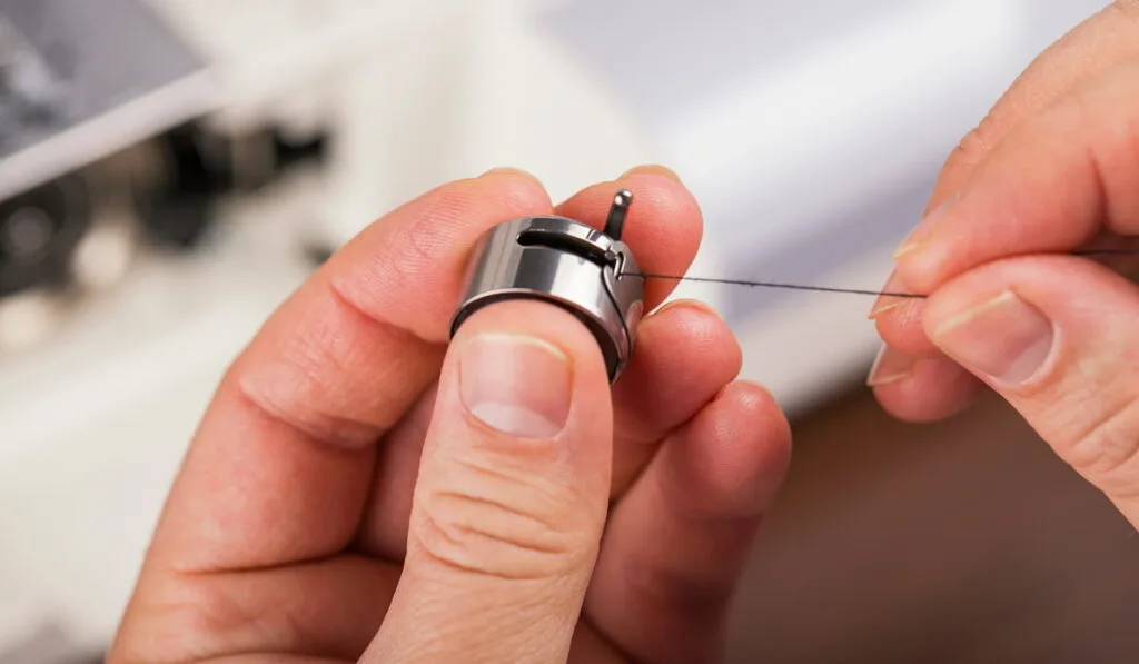 man holds a bobbin case from an inserted bobbin in his hands, embed thread.