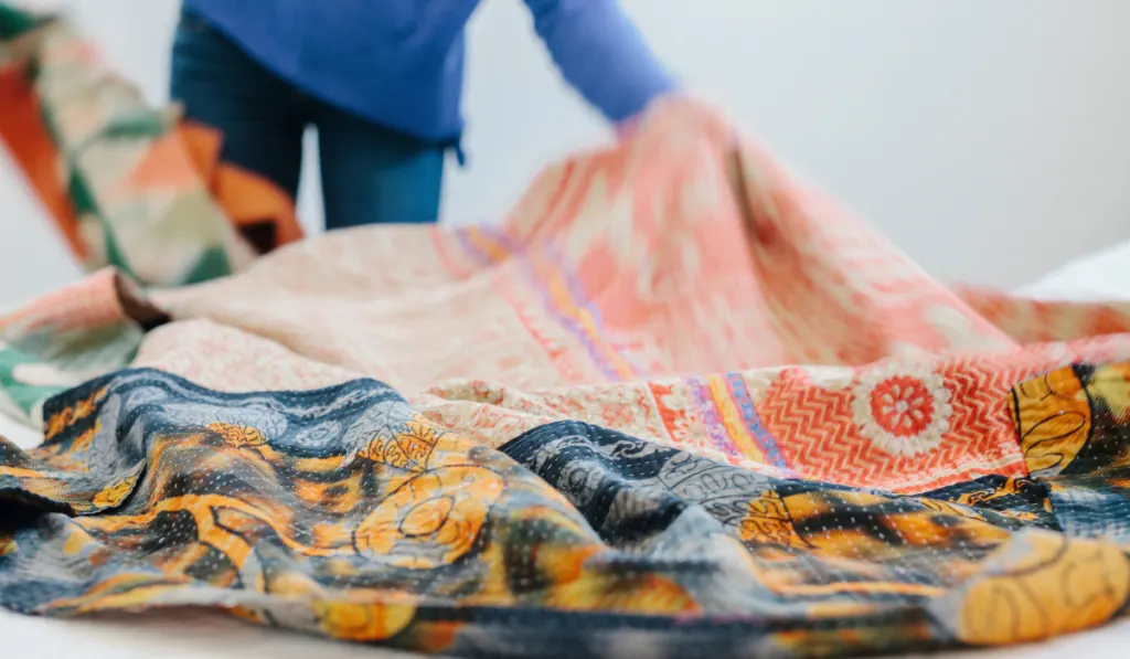 A woman spreading a fabric quilt over a bed in a bedroom.
