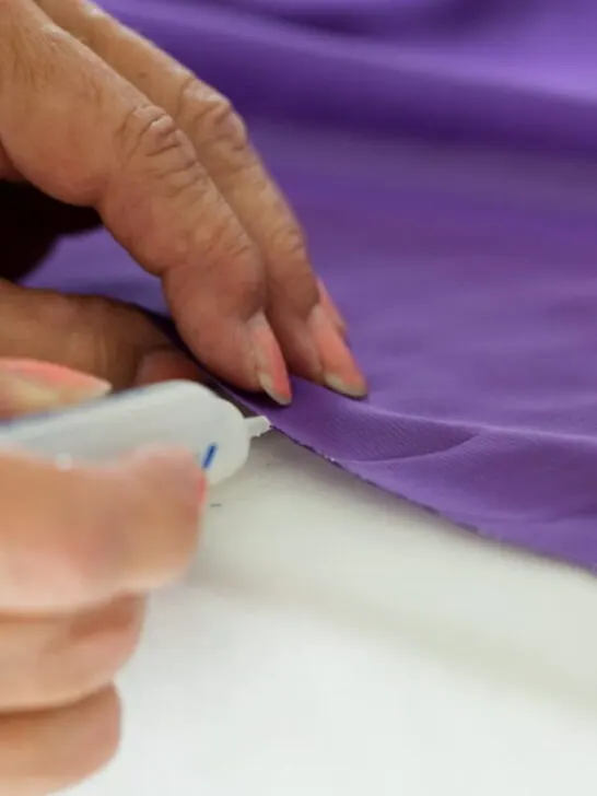 Woman's hands using fabric glue on purple garment - ss220920