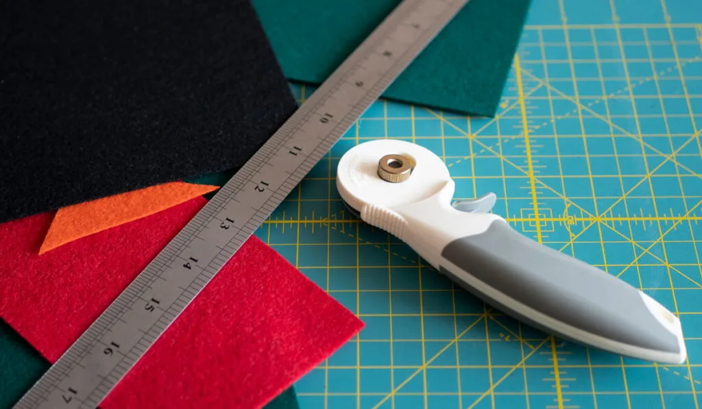 Multicolored felts, a rotary cutter and a ruler on the cutting mat