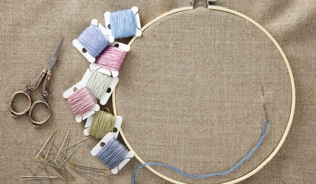 Embroidery supplies, floss, vintage scissors, wooden hoop and needles with cotton linen cloth in hoop