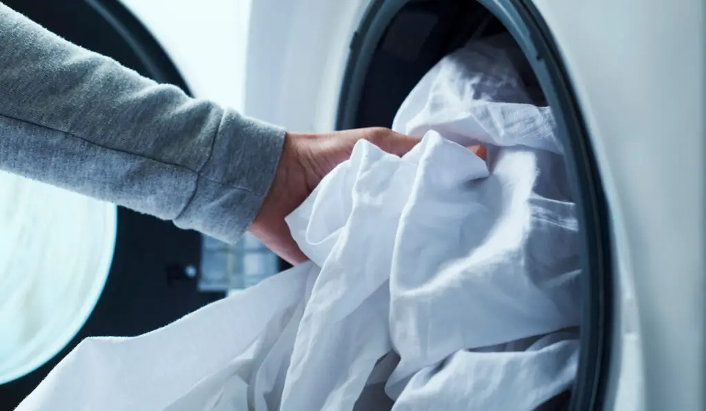 Man putting white bed linen into the washing machine 