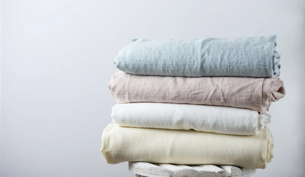 Natural linen fabrics in pastel colors on top of a wooden chair in light background