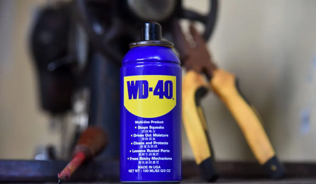 WD-40 oil, with a tong and screw driver placed on the old sewing machine