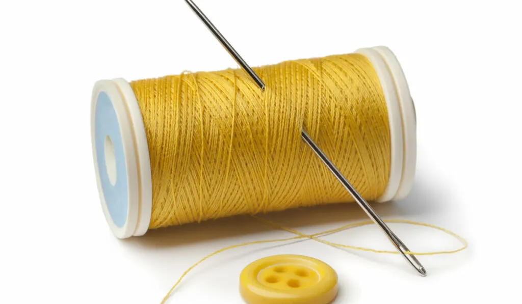 Yellow bobbin, needle and button on white background
