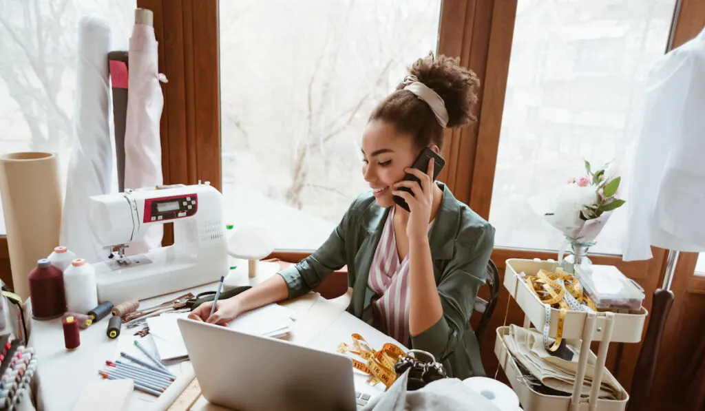 Young woman tailor with her sewing machine talking someone on her phone