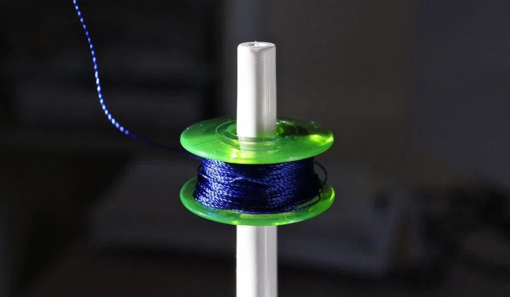 close-up of yellow-green bobbin with deep blue rayon thread against black background