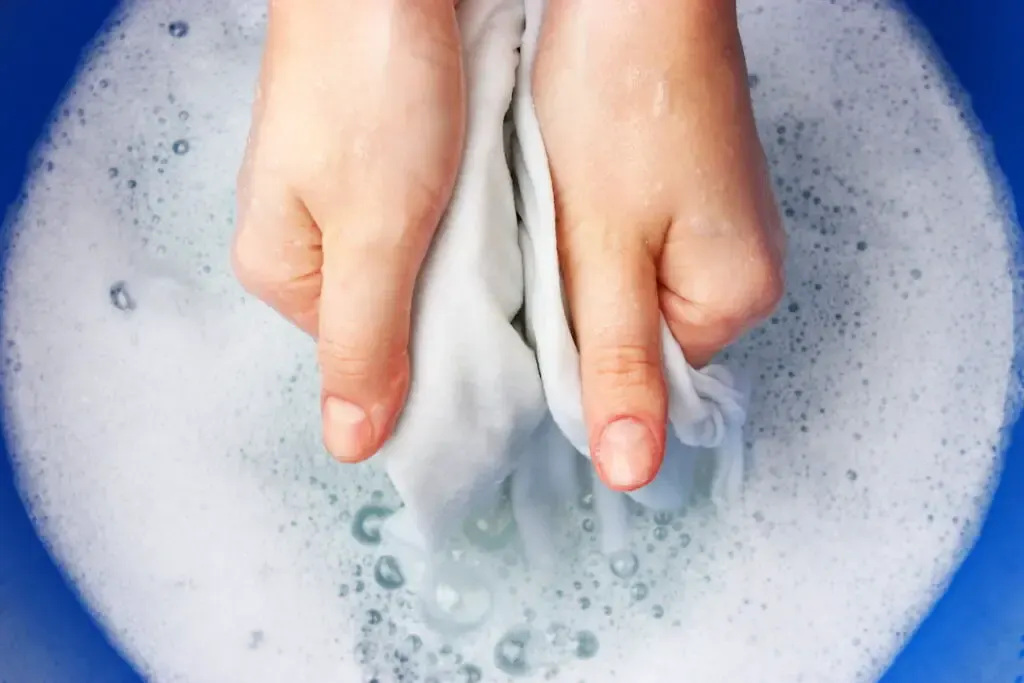 A woman washes clothes by hand in soapy water