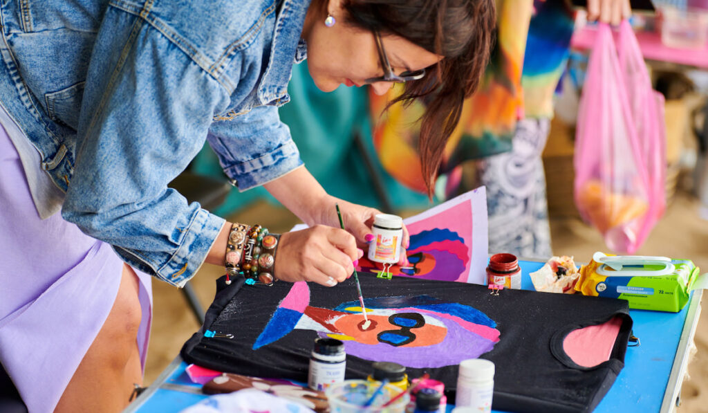 Female artist painting on black t-shirt using brush and fabric paint