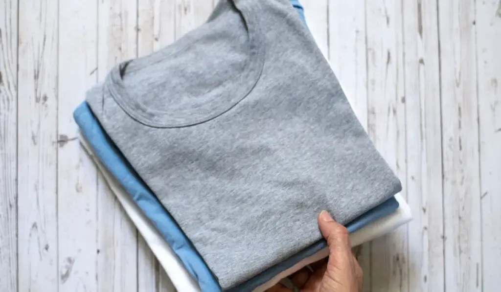 Hand holding folded pastel-colored t-shirts on wooden background