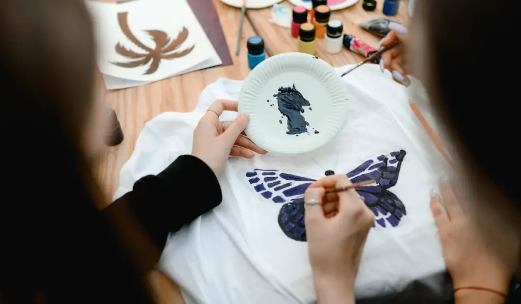 Ladies painting white tshirt using fabric paint on a table