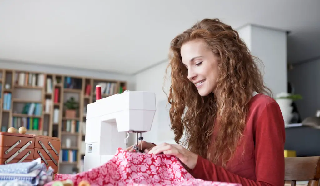 Smiling woman at home using sewing machine