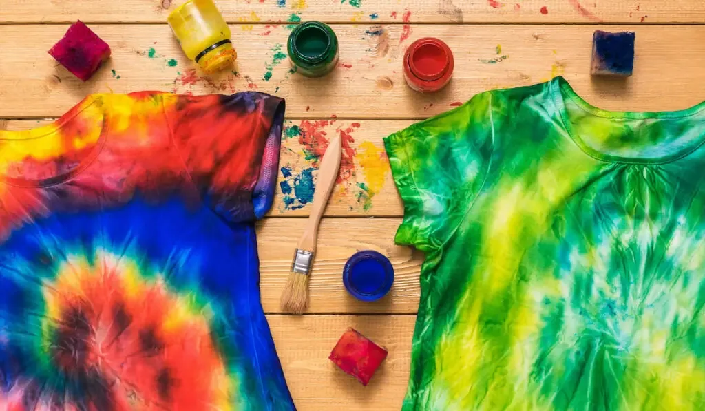 Two tie dye shirts and a fabric painting kit on a wooden table