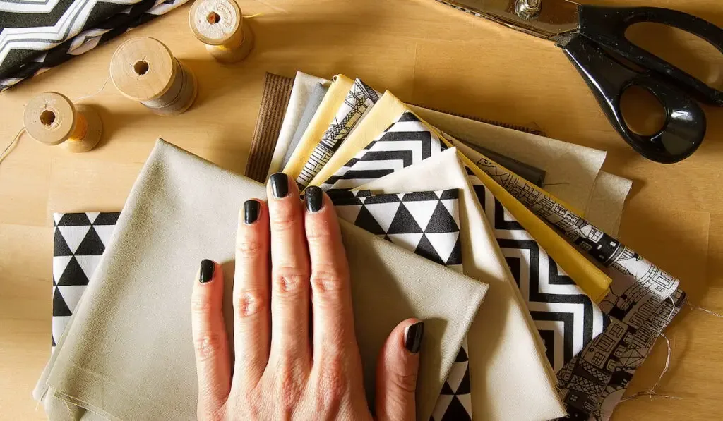 modern quilt fabrics with sewing spools, scissors and woman hand on the wood table
