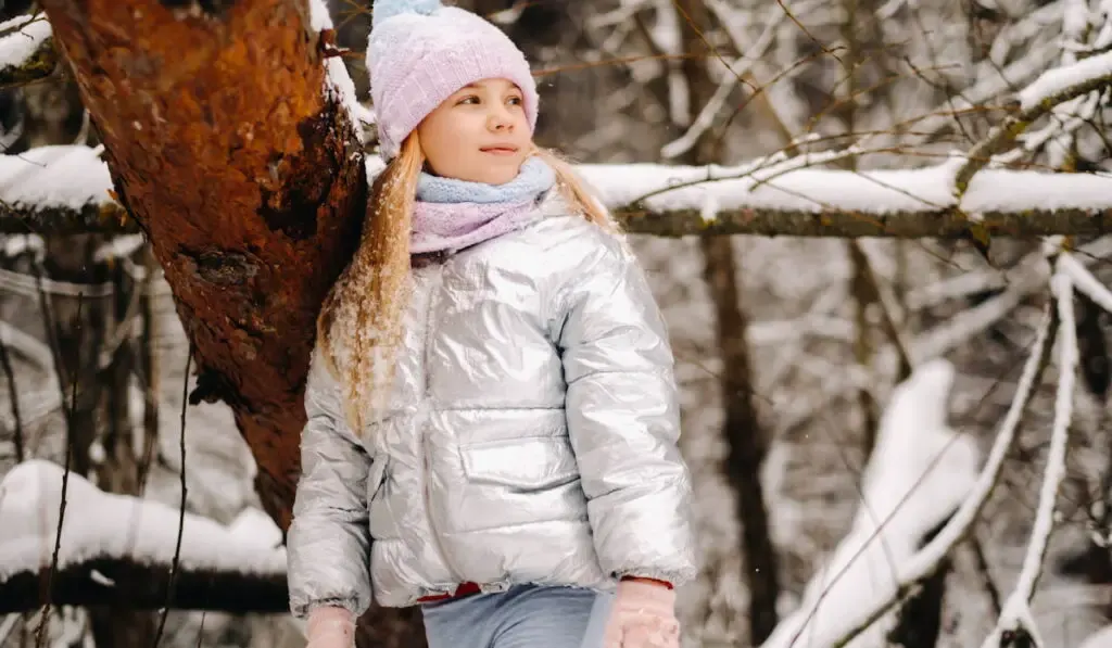 a little girl in a silver jacket in winter goes outside in winter