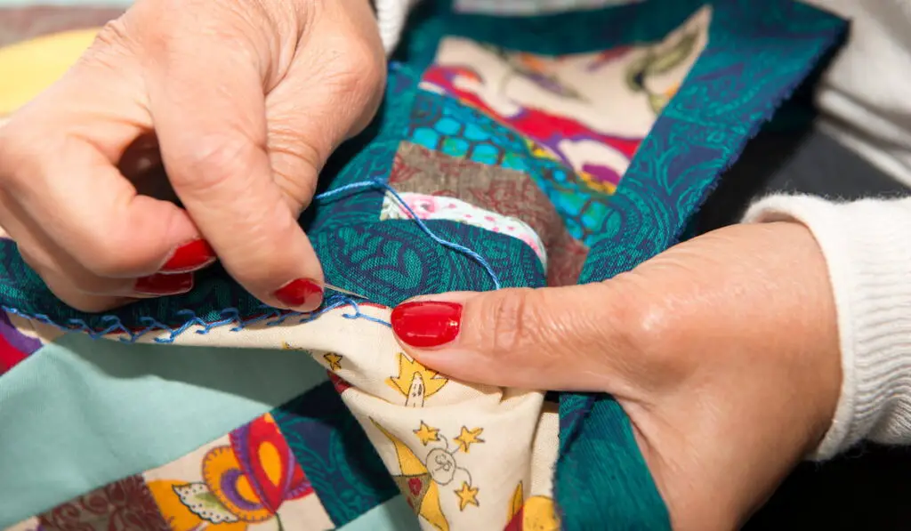 close up photo of woman stitching a quilt 