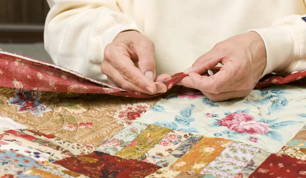 woman stitches by hand the binding to finish a quilt.