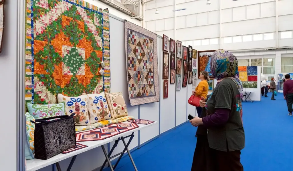woman is looking at a patchwork quilt hanging on a wall in the exhibition hall