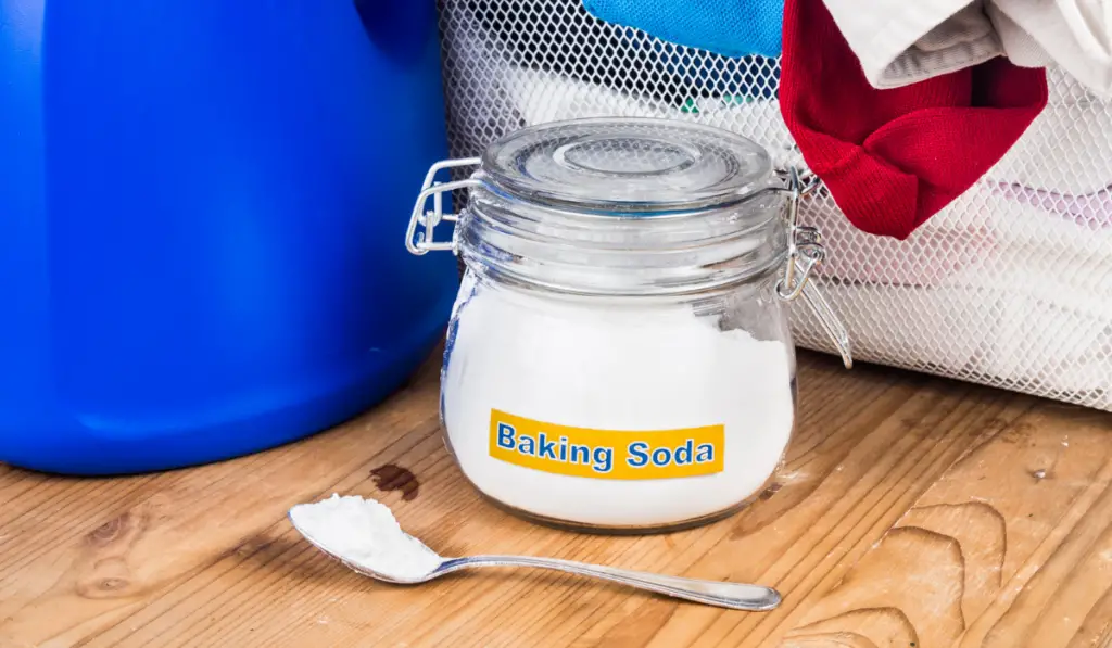 Baking soda with detergent and pile of dirty laundry.
