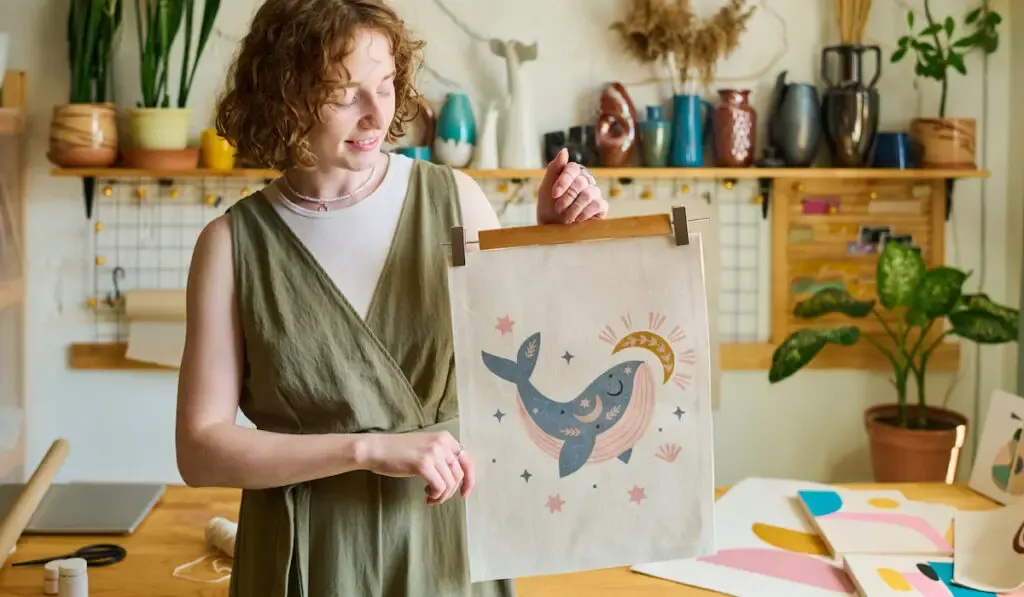 Happy young female artist showing her handmade embroidery of whale on craft hanger