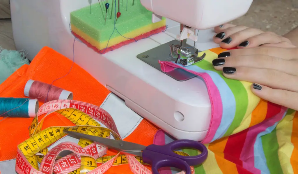 woman sewing a multi-colored fabric, measuring tapes, threads and needles beside the sewing machine